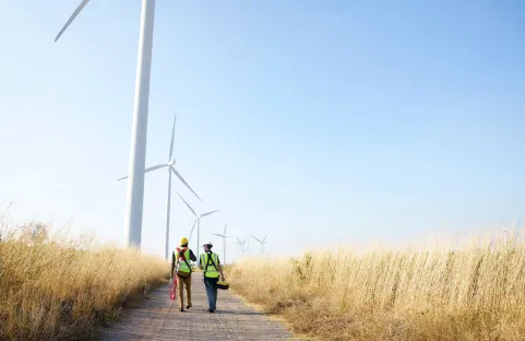 Dos trabajadores especializados frente a unos aerogeneradores terrestres en un campo de trigo